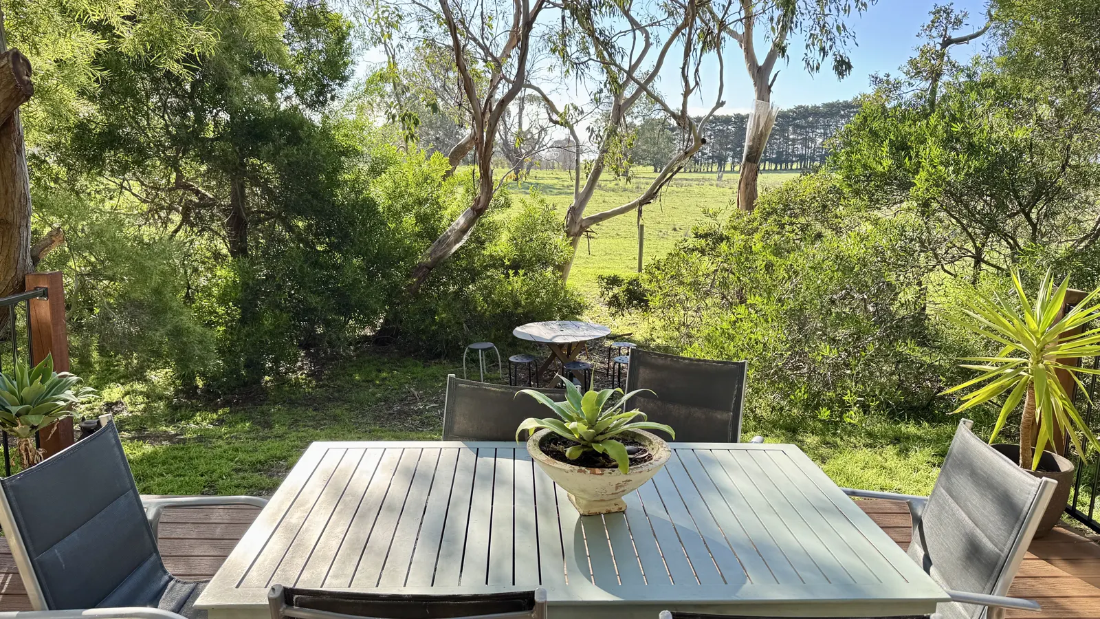 Private timber deck with an outdoor dining table surrounded by leafy trees — Three-bedroom Villa 115, Cowes, Phillip Island