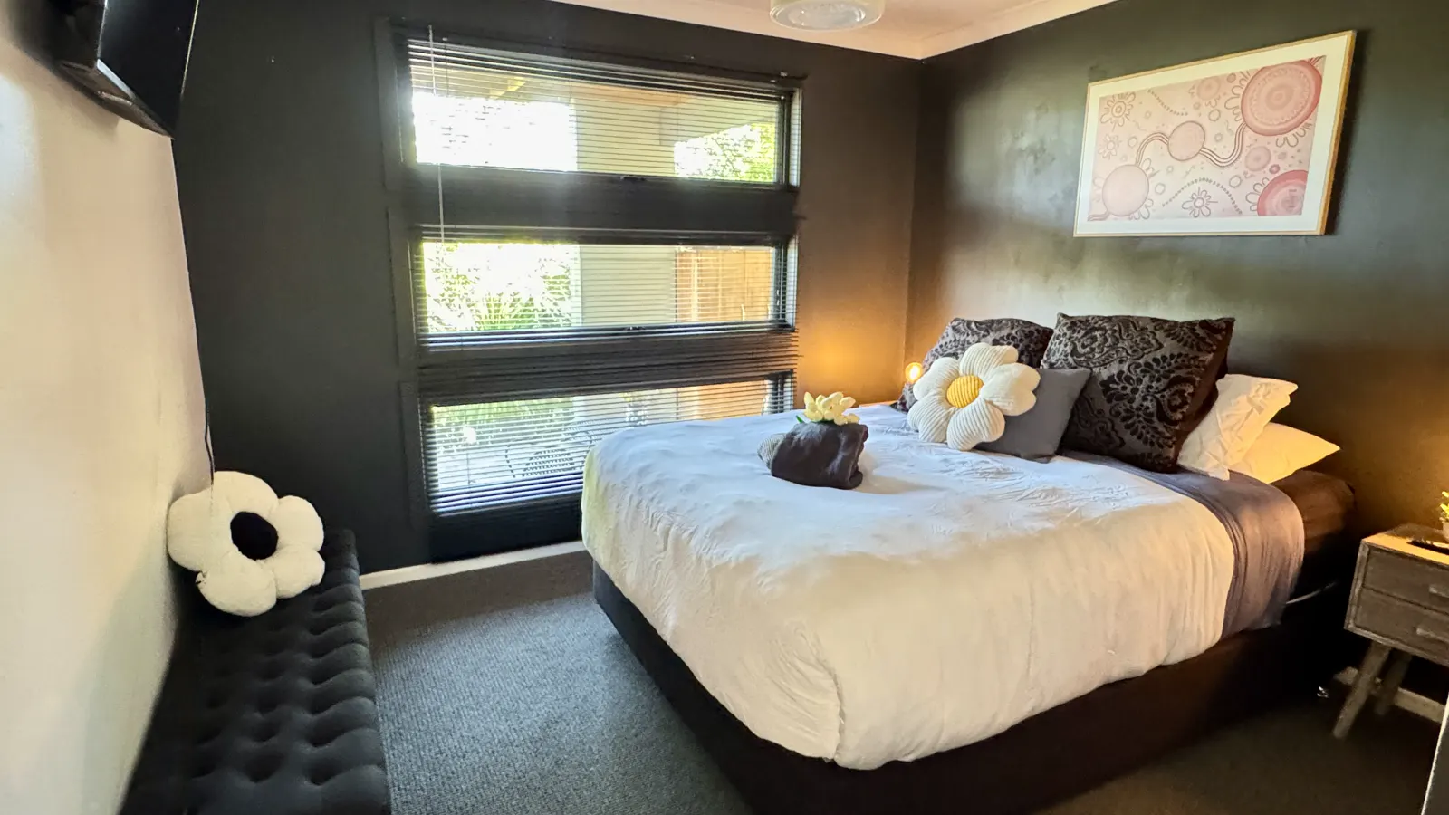Bedroom with a white quilt and decorative flower cushions beside a sunny window — Coastal Tones holiday home, Cowes, Phillip Island
