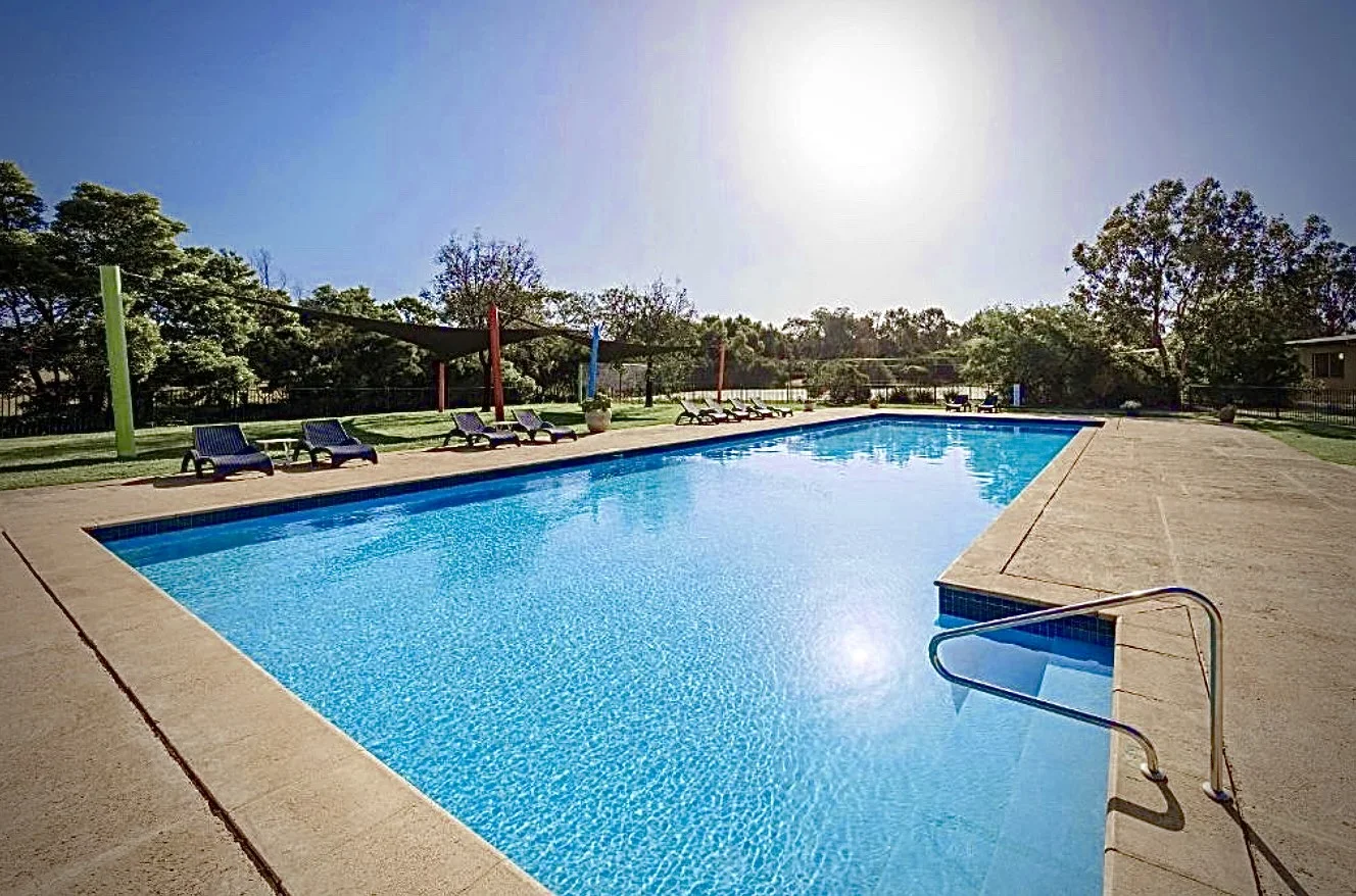 Outdoor resort swimming pool with sun lounges and surrounding trees
