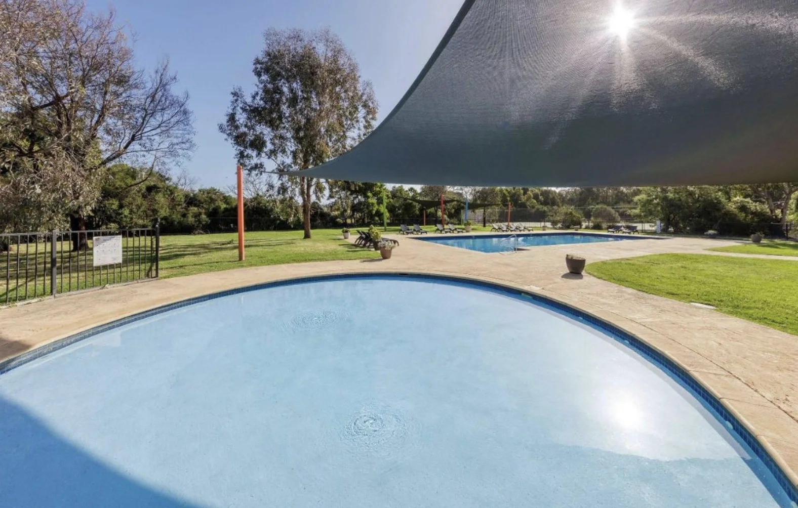 Circular resort pool beneath a shade sail with the larger outdoor pool beyond
